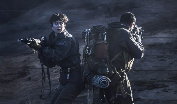 A woman and a man, back to back with their guns out. This is a still from the film Alien: Covenant
