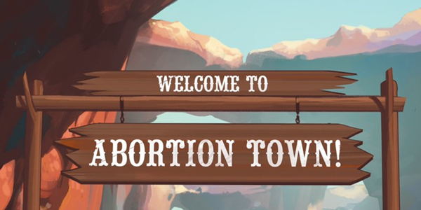 An old west style sign, it reads "welcome to abortion town" with  backdrop of hanging rocks. This is a still from the 25th anniversary edition of Saga