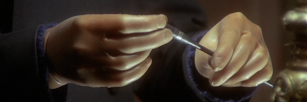 A mans hands, holding an acupuncture needle. This is a still from the film The Black Belly of the Tarantula