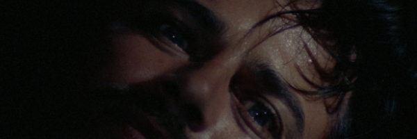 A close up of a mans face, his eyes framed by the edge of the image and hidden in darkness. This is a still from the film a Short Night of Glass Dolls