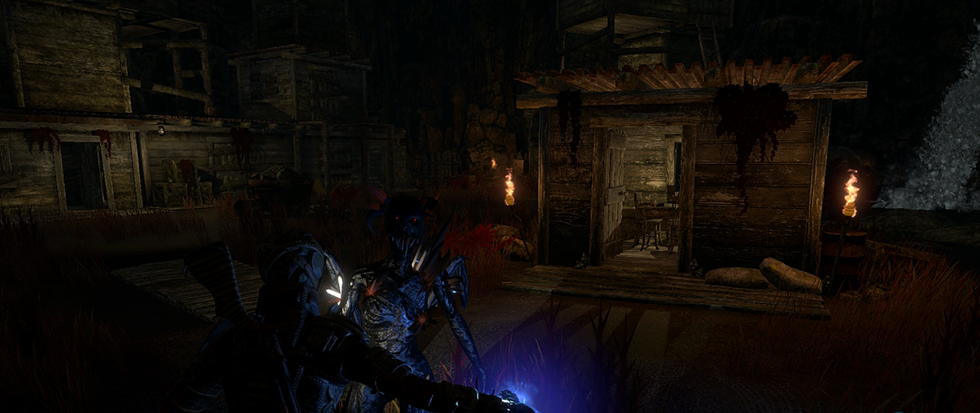 A bright blue demonic figure standing next to a burst of blue light with a wooden cabin in the background.
