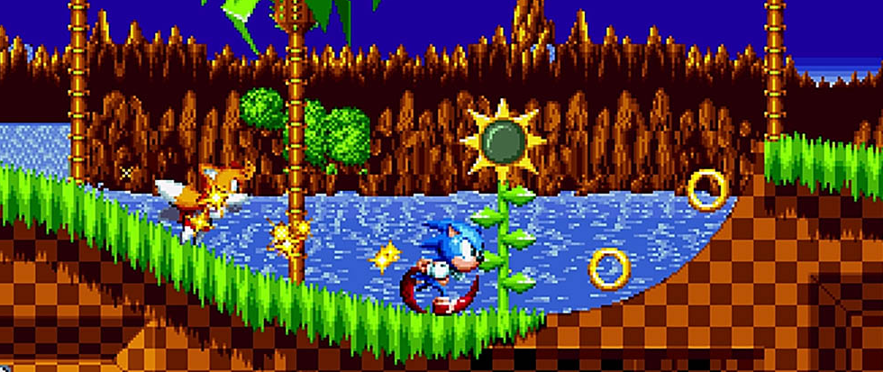 Sonic, his legs a circle of red below him, runs along a green rolling hill in a pixel art style. This is a screen from Sonic Mania.