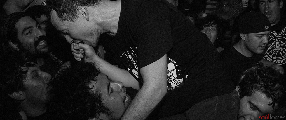 A sweaty man in a black shirt singing into a mic and being carried by a crowd. This is a still from Touche Amore.