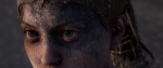 A womans eyes peer out from a blue painted face, her hair running in locs behind her head. This is a still from Hellblade; Senua's Sacrifice