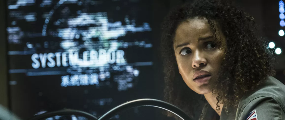 A woman with curly, natural hair and a stunned wary expression on her face looking out with a glitched out screen behind that says "System Error"