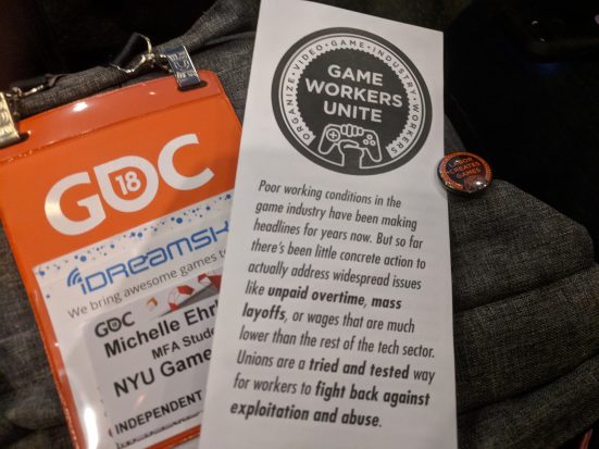 A Game Workers Unite brochure with pin, on top of an orange GDC badge for a NYU Game Center MFA Student, Michelle - text partially hidden.