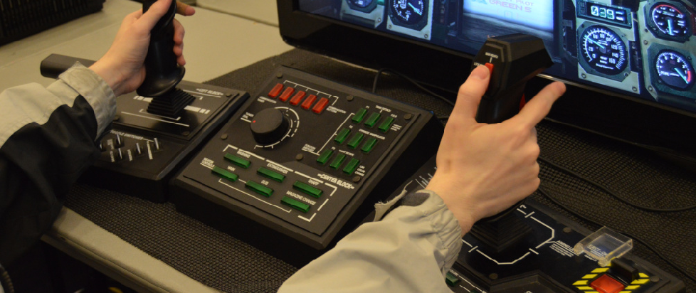 Two hands in a grey sweater holding a Steel Battalion controller, covered in a collection of buttons and dials.