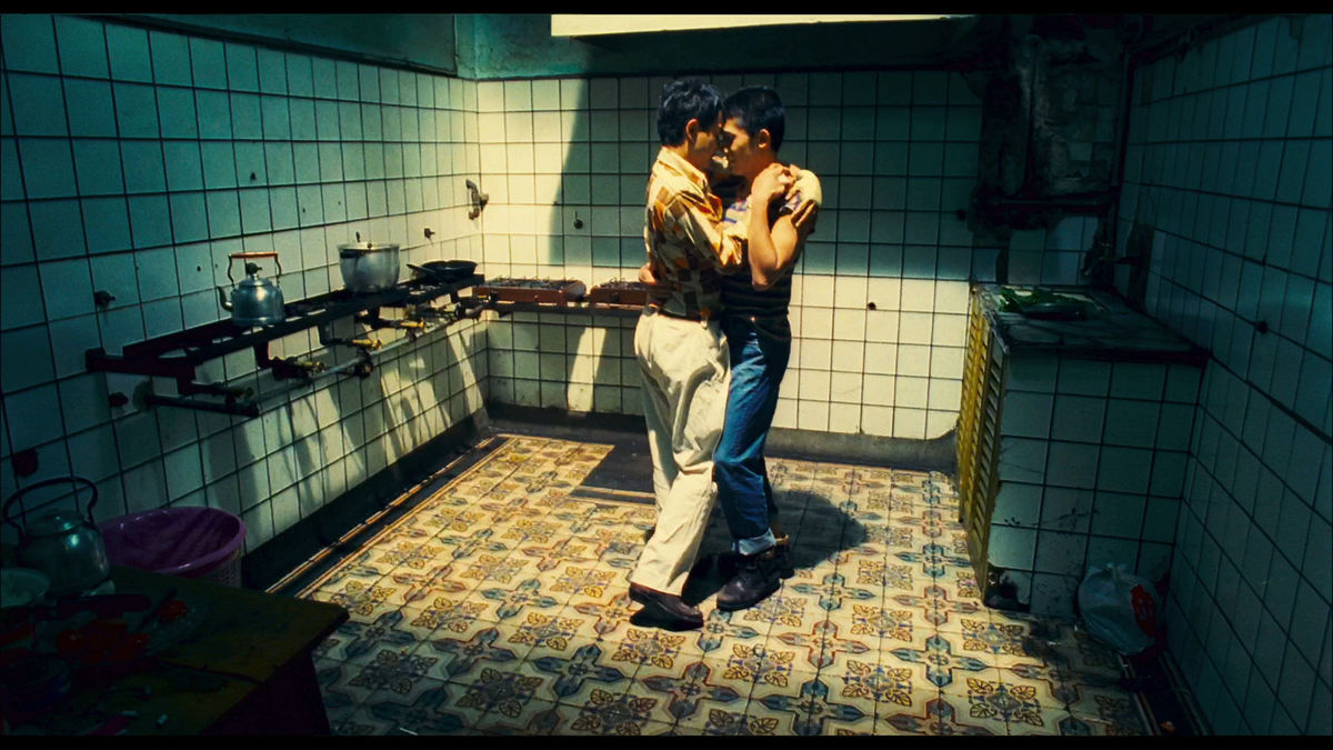 A couple dances in a softly lit kitchen.
