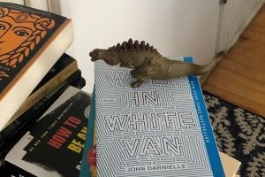 A Godzilla figure stands on top of a copy of Wolf in White Van.