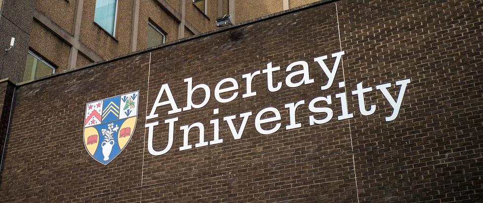A sign bearing the shield and name of Abertay University hung on the side of a brick building.