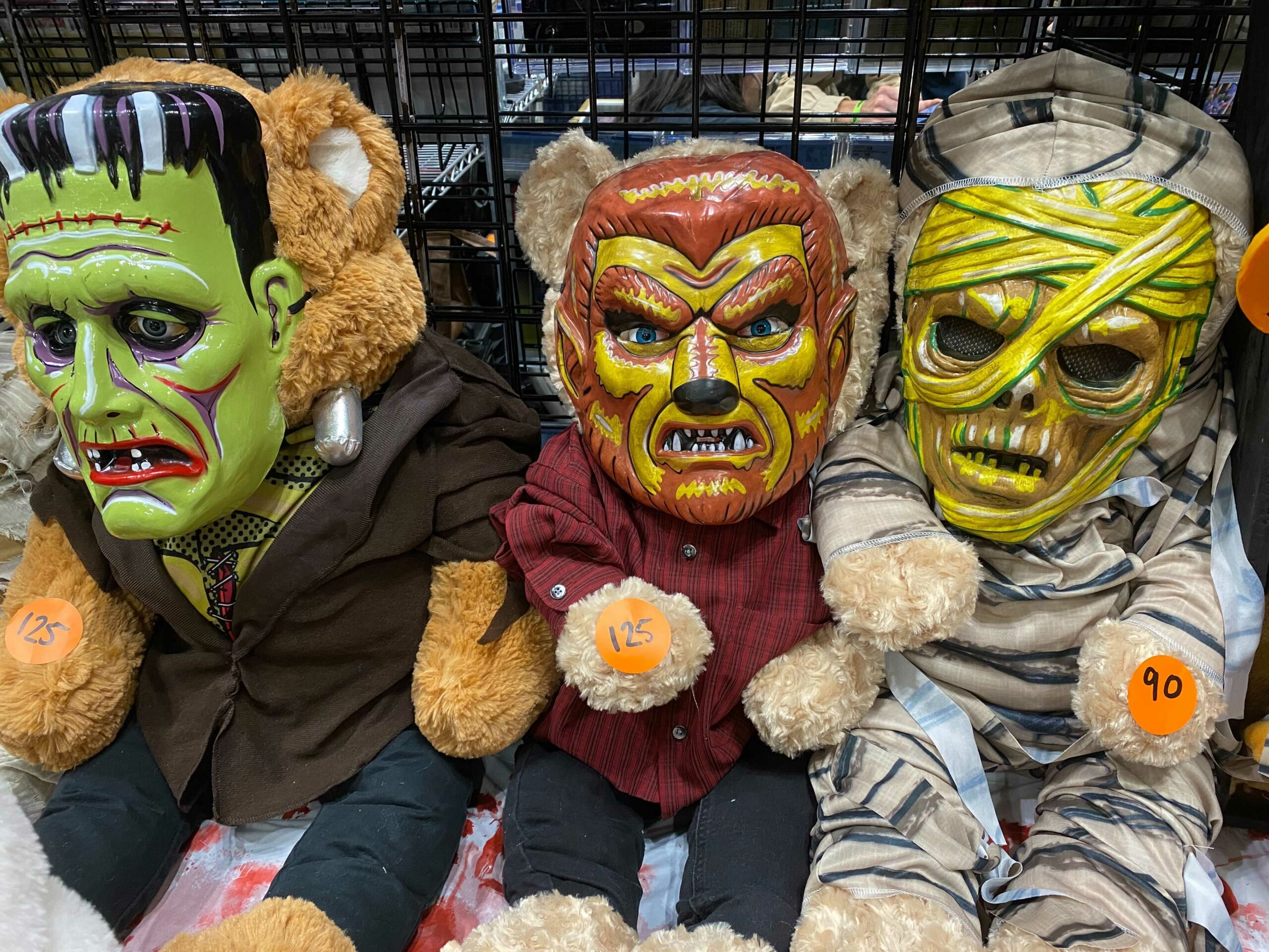 Three teddy bears dressed up with Halloween masks to look like monster: Frankenstein's creature, a wolfman, and a mummy.