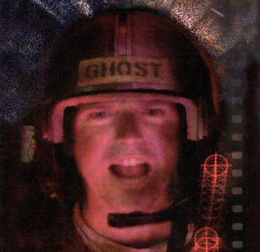 A still-frame close-up of a pilot's face from the videogame Sewer Shark. He is yelling into his communicator and his helmet has a tag that reads "Ghost." 