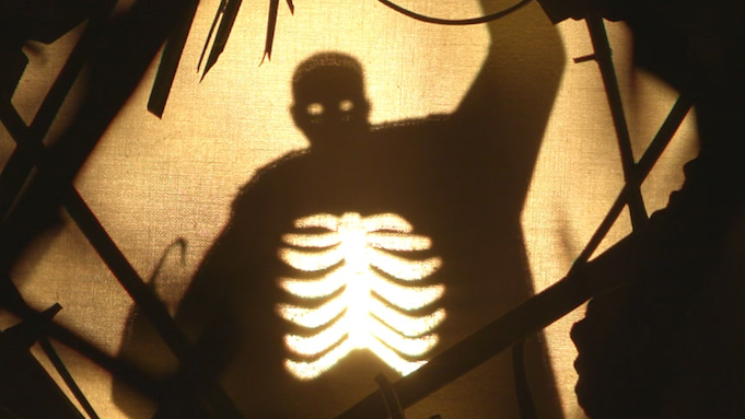 A shadow-silhouette of a man, as if made with paper, with glowing cutouts for eyes. In his chest another cutout reveals his whole ribcage.