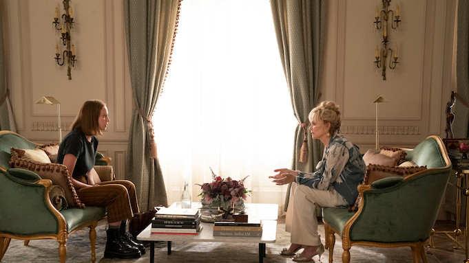 Two women sit in an opulent living room. One is middle-aged and dressed casually but expensively, the other is young and wears combat boots.