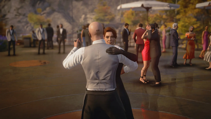 A bald man dances with a woman in a long black dress at an outdoor party. A barcode is tattooed on the back of his head.