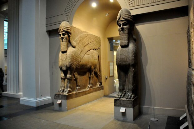 Two stone lamassu sculptures framing an arched doorway in a museum.