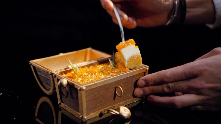 A close-up of someone placing golden honeycomb candy into a treasure chest made of chocolate.
