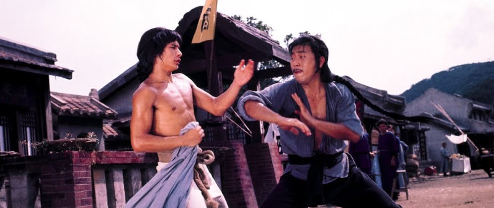 A still from the movie 5 Shaolin Masters showing a bare chested man foisting off a man in a martial arts pose.