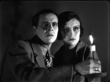 A Still from Film 2 past El fantasma del convento (The Phantom of the Monastery), where a man and a woman are draped in shadow, holding a candle and staring off screen in fear and confusion