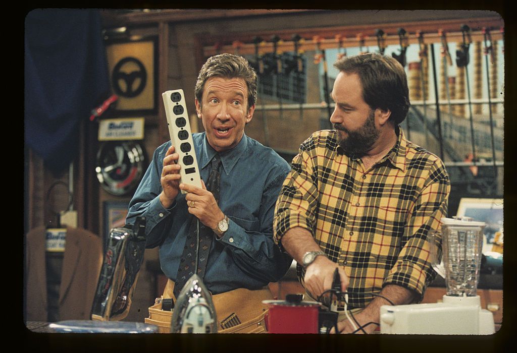 In a still from the 90s television show Home Improvement, Tim "The Tool-Man" Talyor holds up a power strip while his assistant Al Borlen looks on warily.
