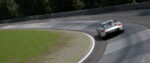 A silver sports car makes a left-banked turn on a professional racetrack. Lush trees line the outer perimeter of the track.