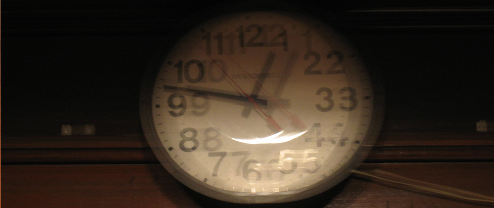 A blurry photo of a clock reading quarter-to-twelve. It looks as if the viewer is the one with blurred vision.