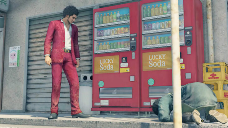 In a screenshot from Yakuza: Like a Dragon, a many in a stylish berry-colored suit stands above another man groveling in the street. Beside them are two soda machines in the same berry hue.