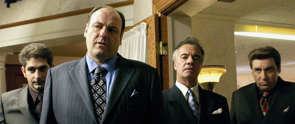 In a still from The Sopranos, four Italian men in well-tailored suits stare down the camera.