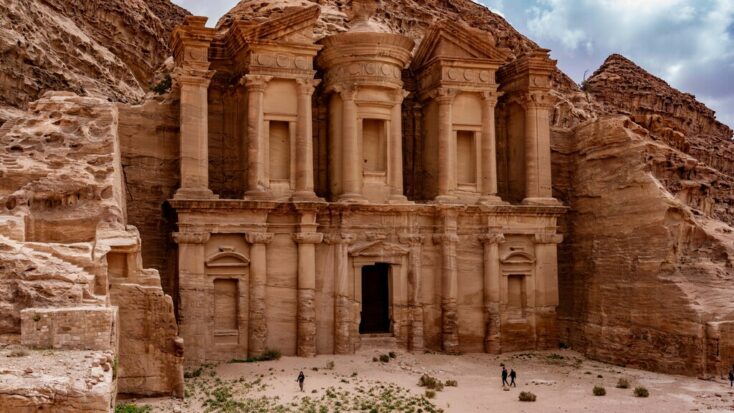 A front view of Al Khazneh, a temple with an ornate, Greek-style facade carved into a rose-colored cliff at Petra in Jordan.