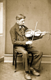 A sepia-toned photograph of Myllarguten, a seated Norwegian man gazing down at the fiddle he's holding. 