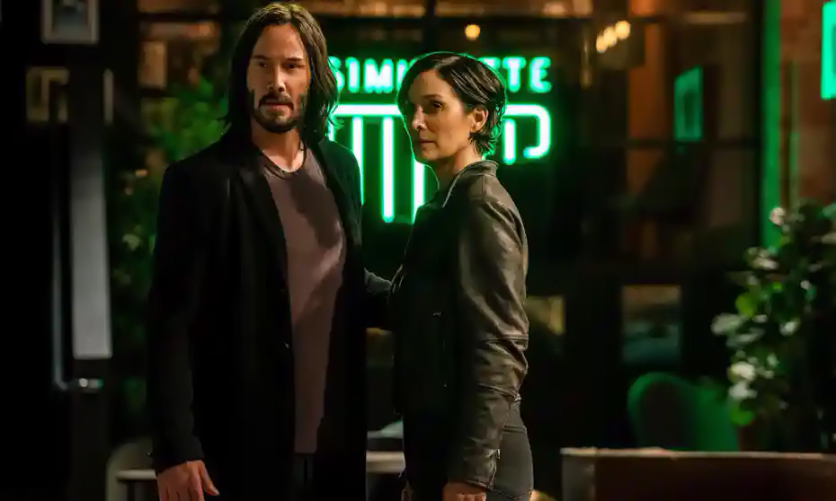 In a still from The Matrix Resurrections, Neo and Trinity stand close together in a coffee shop.