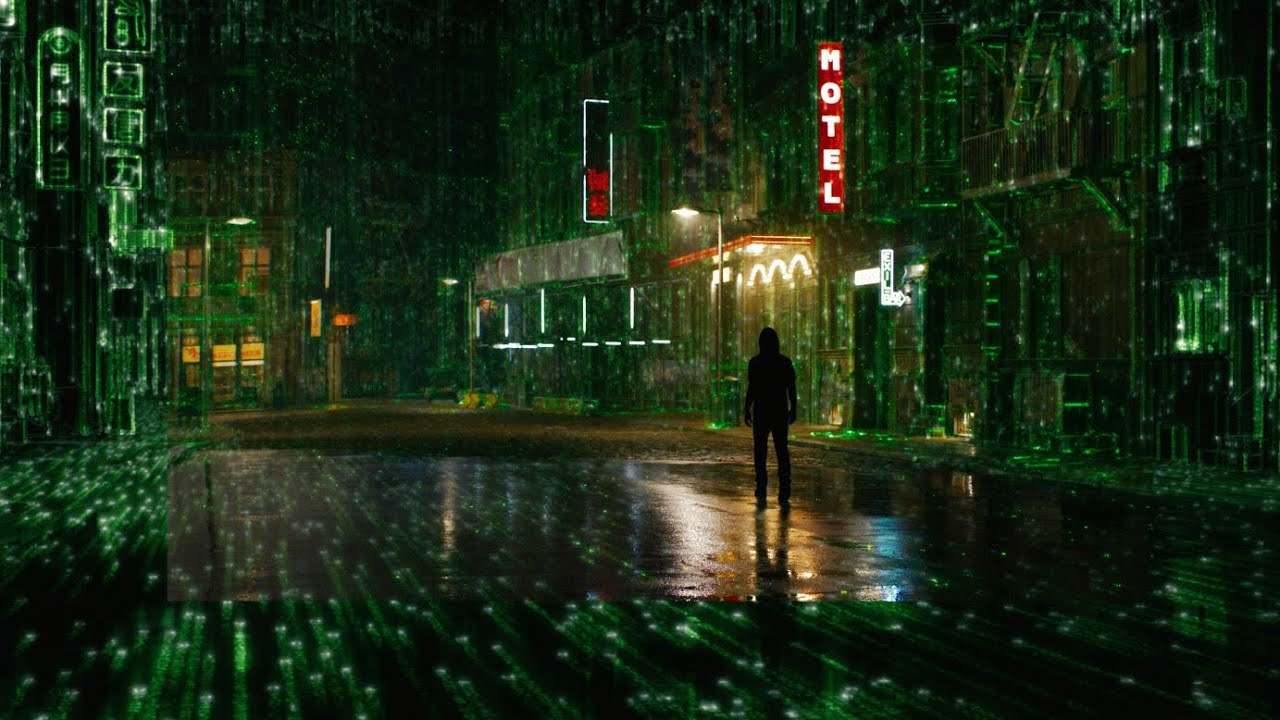A still from The Matrix Resurrections shows Neo as small figure standing on a rain-slicked city street at night. The street and surrounding buildings are comprised partially of The Matrix's signature green lines of code.