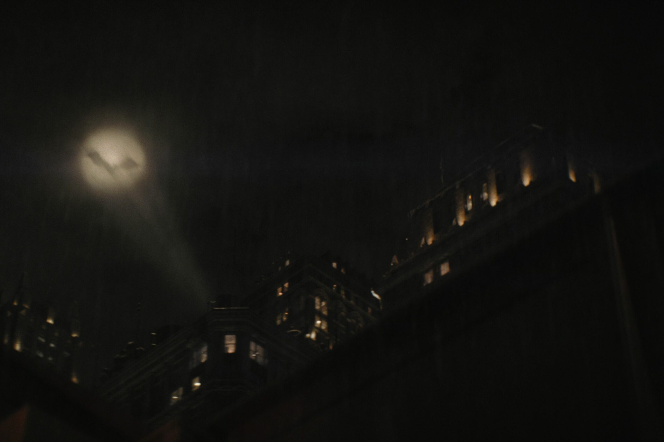 The Bat-signal shines up into a hazy night sky.