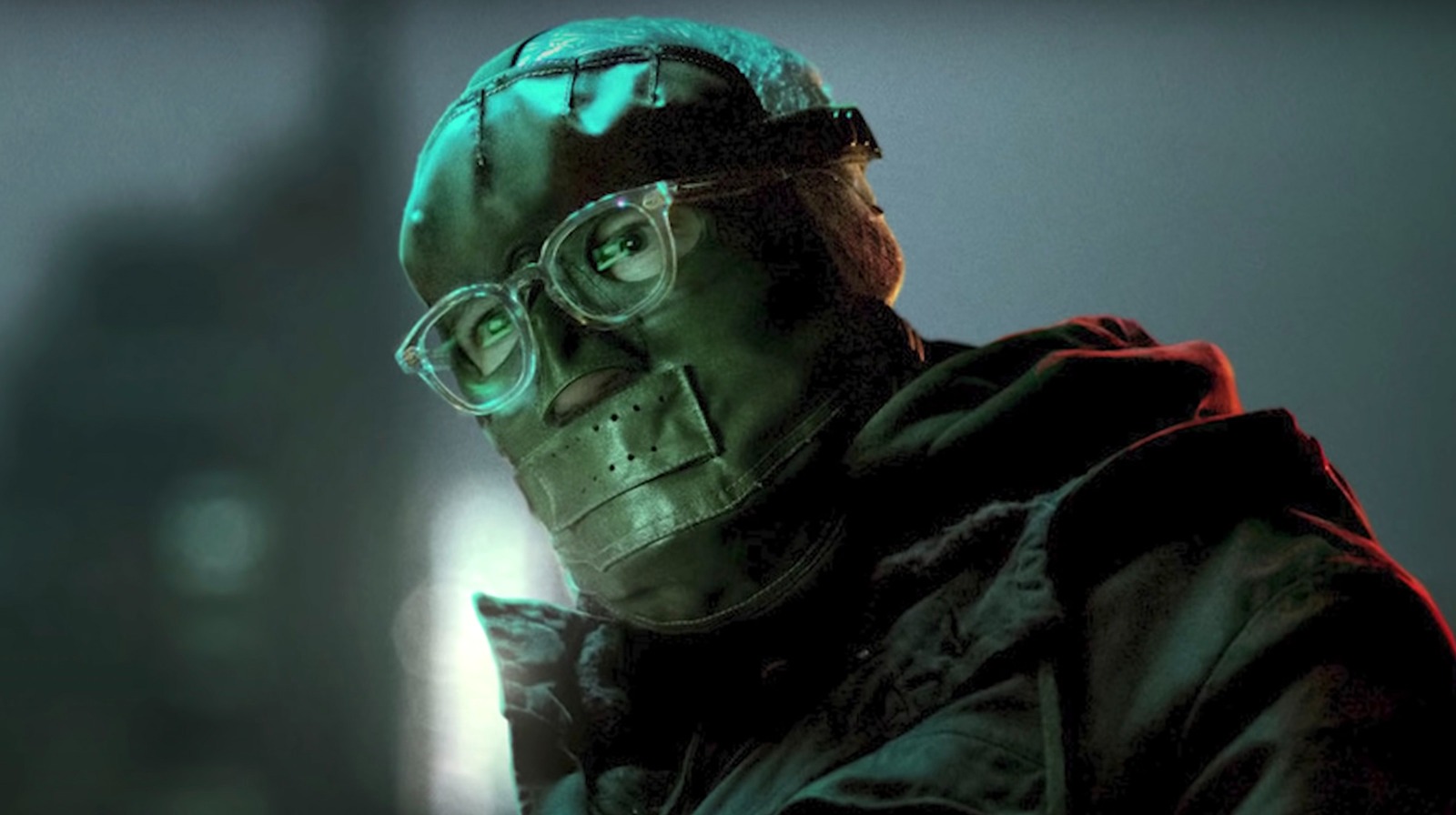 A close-up of Paul Dano's The Riddler from The Batman. He wears a leather mask that covers everything but his eyes. He wears clear-framed eyeglasses over his mask.