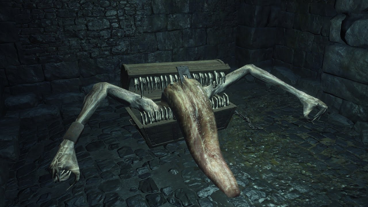 In a screenshot from Dark Souls III, a mimic (a monster that appears as a treasure chest with arms, teeth, and a giant lolling tongue) seems to lurch towards the viewer.