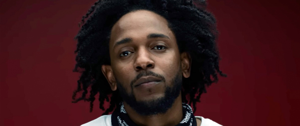 A close-up portrait of Kendrick Lamar, a bearded man with dreadlocks.