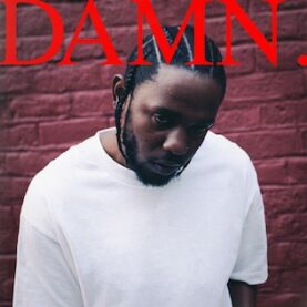 Cover art for Kendrick Lamar's DAMN., which is a photograph of a bearded Lamar standing in front of a red brick wall wearing a white t-shirt.