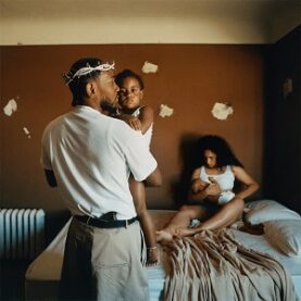 Cover art for Kendrick Lamar's Mr. Morales & the Big Steppers, a photograph of Lamar with his fiancée and two children. She sits on a bed breastfeeding an infant while Lamar stands with his back to the camera, holding a toddler and wearing a crown of thorns.