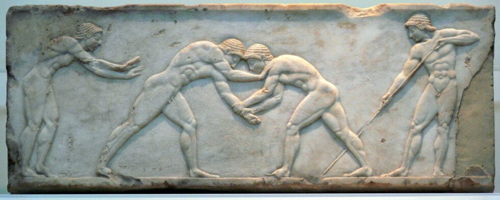A stone frieze of two Greek men wrestling while a Greek woman and another man cheer and keep score, respectively.