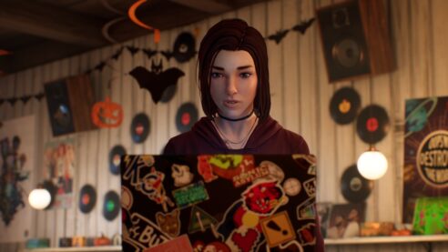 a different young woman with short hair sits in a cool coffee shop with seven inch records on the wall and a bat decoration hanging from the ceiling while she stares pensively at a laptop covered in stickers
