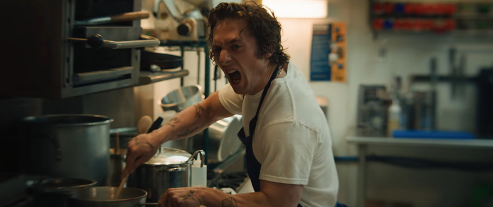 A chef in a fast-casual Chicago restaurant kitchen, screaming intensely while simultaneously cooking.