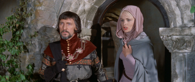 Young Peter Cushing in all his Sheriff Finery stands next to a robed blonde lady, both looking a little shocked or bemused by something offscreen