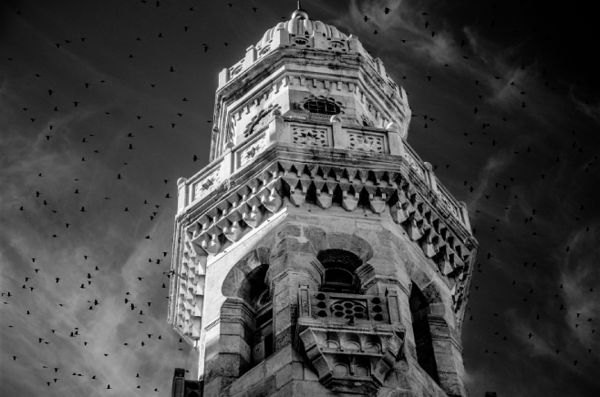 A show of an imposing tower from Dark Souls surrounded by black birds and wispy clouds, with many small ornaments and open windows