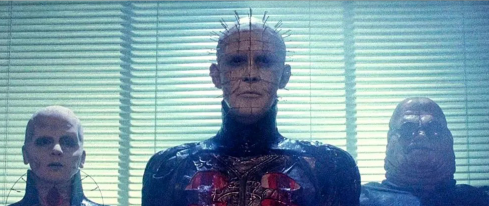 Hellraiser's Female Cenobite, Pinhead, and Butterball stand in front of starkly back-lit binds.