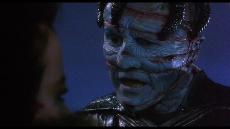 Hellbound: Hellraiser II's Dr. Channard after being transformed into a cenobite. His bluish skin is lacerated in horizontal lines across his face and several black plastic tubes lead out of his head.