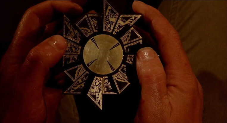 A close-up of hands holding The Lament Configuration, a golden puzzle box from the Hellraiser franchise.