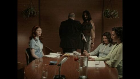One of many scenes from Immortality, featuring a wood paneled and tabled room with a ceramic ashtray just to nail down the late 60's/70's vibe with hanging potted planets, muted colors, and grainy threats
