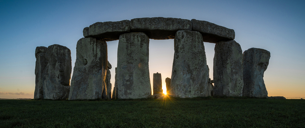 An image of Stonehenge looking majestic as the sun sets behind it, perfectly aligning between two stones.