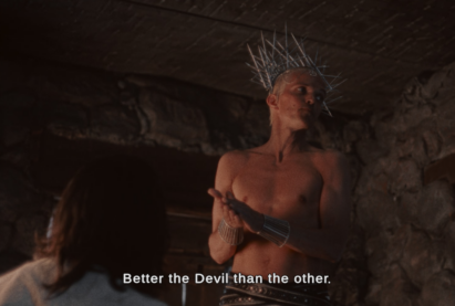 A shirtless man wears a crown of large metal nails and a leather belt, rubbing his hands together while standing over someone sitting below. Subtitle says "Better the Devil than the other."