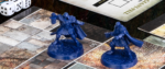 A shot of two mini figures from Warhammer: Lost Relics, a robed warrior brandishing a lamp and a hammer-wielding cleric prepaing to strike, both standing on a sample of the various ground textures available to dungeon crawl through